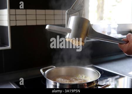 Spaetzle dough is pressed through a hand press. Stock Photo