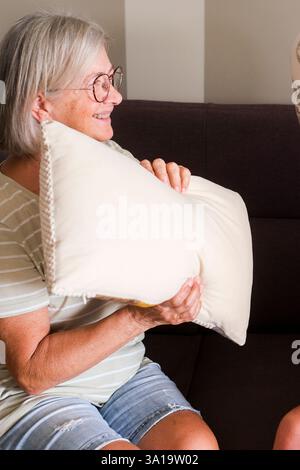 An older couple enjoying a playful pillow fight on the sofa at home, demonstrating a youthful spirit and joy in their golden years. Their fun and affection reflect a loving and active life together in retirement Stock Photo