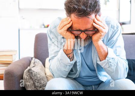 Close up unhealthy stressed adult man wearing glasses touching forehead, suffering from headache, tired overworked freelance, husband massaging temples, feeling pain, health problem. Mature stressed Stock Photo