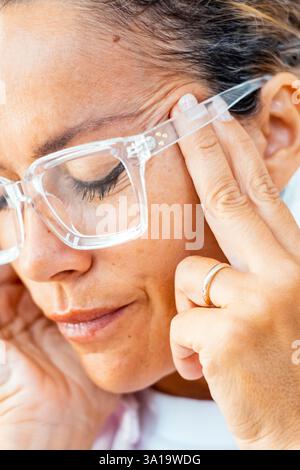 Close up portrait of upset painful mature woman touching temples for migraine head ache or stress overwork condition. Bad day and fever flu symptoms. Wearing glasses. Adult female massaging head Stock Photo