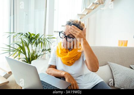 Frustrated sad woman feeling tired worried about problem sitting on sofa with laptop, stressed depressed girl troubled with reading bad news online, email notification about debt or negative message Stock Photo