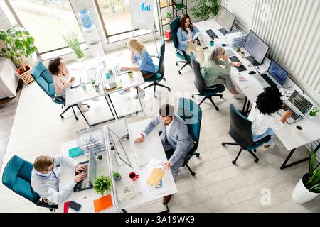 Modern open-plan office with diverse professionals collaborating on computers during daylight hours, top view Stock Photo