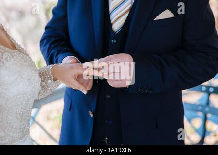Bride and groom share a tender moment as they exchange rings, celebrating their love in a beautiful outdoor location. Stock Photo