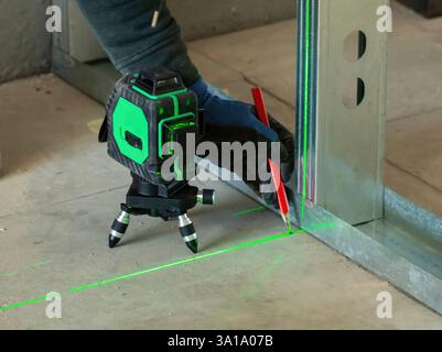 Construction worker using a cross line laser level and marking a red line on a concrete floor Stock Photo