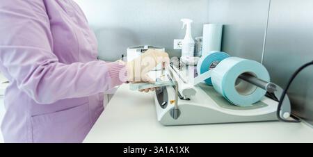 Nurse wearing gloves packing medical instruments using a vacuum packing machine in a dental clinic Stock Photo