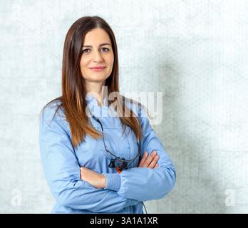 Confident female dentist wearing binocular magnifier posing with arms crossed in dental clinic Stock Photo