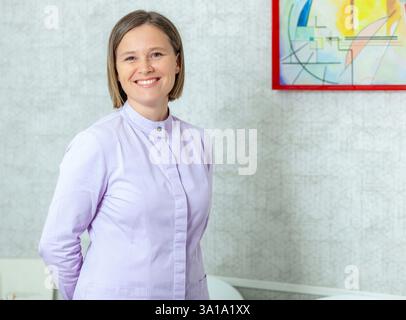 Smiling professional dentist posing confidently in her modern office, showcasing expertise in dental care and patient service Stock Photo