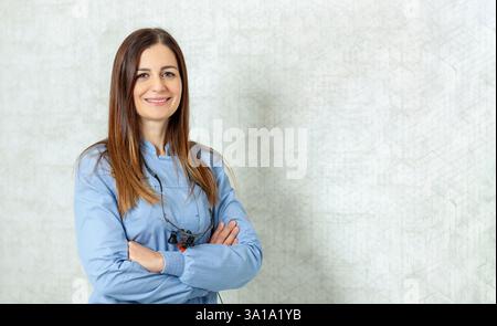 Confident female dentist wearing binocular magnifier smiling with arms crossed in dental clinic Stock Photo