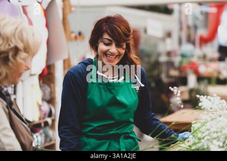 Two florists work in a nursery. Couple work in the gardening business on an ordinary working day. In the photo a blonde woman and a young woman with red hair. Authentic images. Stock Photo