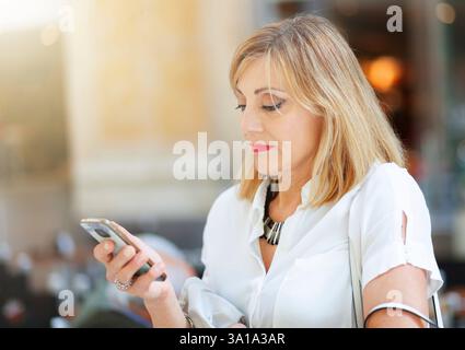 Adult and elegant woman with blonde hair uses the smartphone Stock Photo