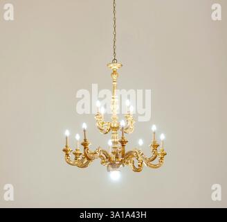 Golden chandelier with its lights on is hanging from the ceiling, illuminating the room with warm light Stock Photo