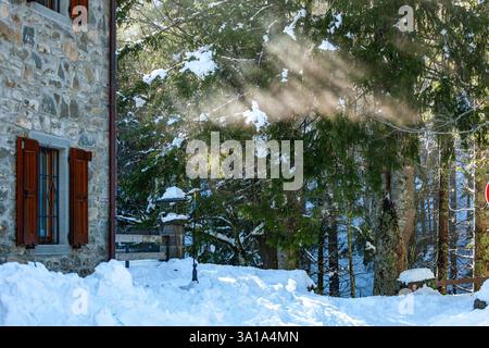 Winter and snowy rural scene with stone house and sun rays breaking through the trees. Stock Photo