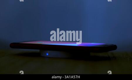 Wireless induction charger base for mobile phone. Moonlight scene while a smartphone is placed on the dock for charging. Stock Photo