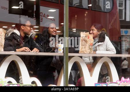 Three people, likely students, are enjoying McDonald's food at a McDonald's restaurant in Bromley London, UK.  They are seated at a window table, with Stock Photo