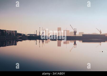 Trucks and dockside cranes reflected in still water through mist at Chatham Maritime, on the Medway delta, UK Stock Photo