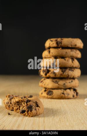 A stack of chocolate chip cookies sits on a wooden table. A single cookie is missing from the stack Stock Photo