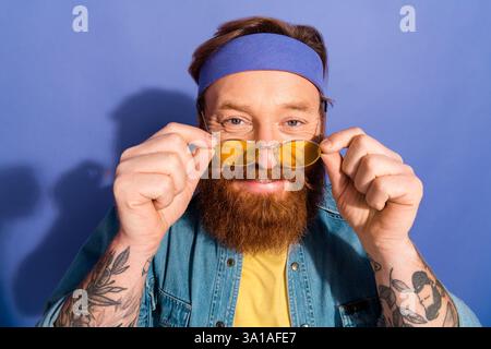 Portrait of a trendy bearded man wearing a denim jacket and headband against a purple background Stock Photo