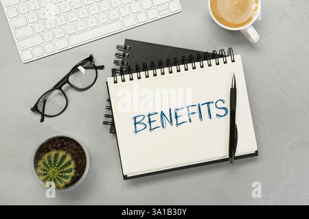 Benefits word in notebook, pen, coffee, eyeglasses and computer keyboard on grey table, top view Stock Photo