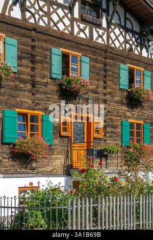 Rettenberg, Gästehaus Stork, old wooden house with half-timbered gable, flowers in front of the windows and green shutters. Stock Photo