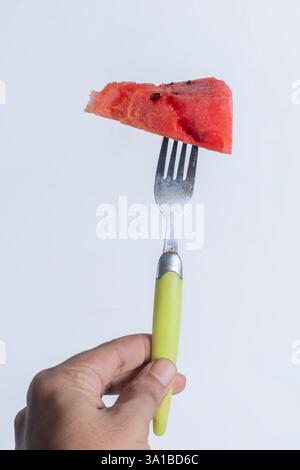 A vibrant and juicy triangular slice of watermelon held on a fork with a yellow handle. ideal for healthy eating and tropical themes. Stock Photo