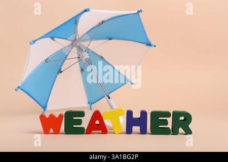 Mini umbrella and word WEATHER made of colorful letters on beige background Stock Photo