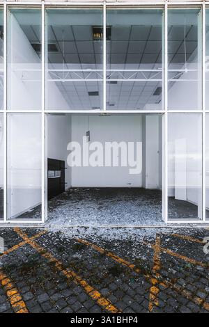 Abandoned commercial building ready for demolishing, with shattered glass at the entrance. Empty interior with white walls, broken ceiling panels, and Stock Photo