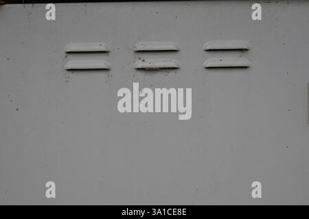A white wall with three holes in it. The holes are in a row and are spaced out Stock Photo