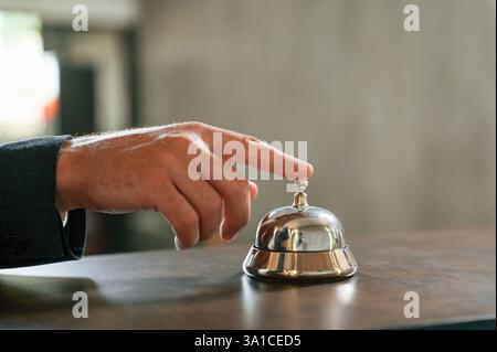 Close up view, using hotel desk bell. A man in a black jacket at the hotel reception. Stock Photo