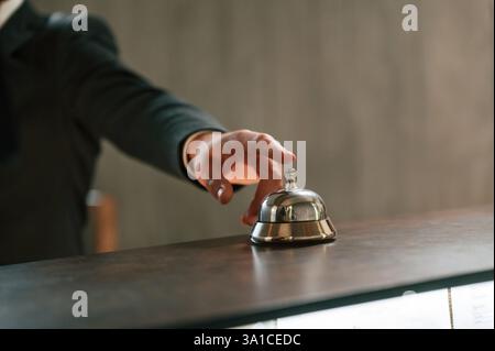 Close up view, using hotel desk bell. A man in a black jacket at the hotel reception. Stock Photo