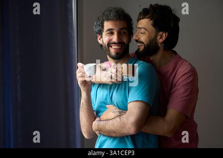 Happy gay couple embracing and drinking coffee by the window Stock Photo
