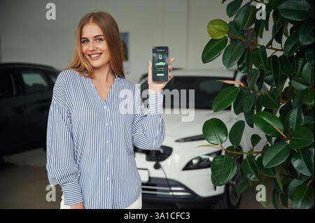 Mobile app interface of charging the electric car. Beautiful woman is indoors. Stock Photo