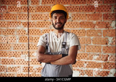 Indoors against brick wall. Handsome Indian man is on the construction site. Stock Photo
