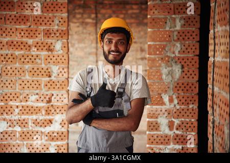Indoors against brick wall. Handsome Indian man is on the construction site. Stock Photo