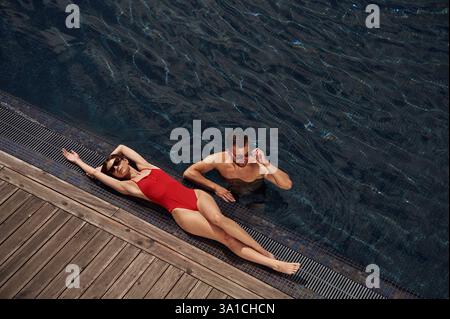 Woman is lying down. Man is in the pool. Stock Photo