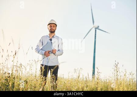 Working by using laptop. Service engineer is on the field with windmills. Stock Photo