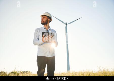 Standing against sunlight. Notepad in hands. Service engineer is on the field with windmills. Stock Photo