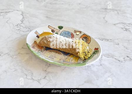 A plate of food with a dessert on it. The dessert is a pastry with a white icing and a sprinkle of powdered sugar. The plate is on a marble countertop Stock Photo