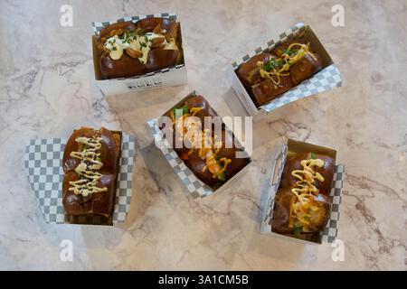 A row of five hot dogs with different toppings. The hot dogs are in paper containers and are arranged in a line Stock Photo