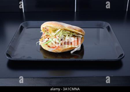 A sandwich with lettuce and tomato is placed on a black tray. The sandwich is sitting on a black surface, and it is a simple yet appetizing meal. The Stock Photo