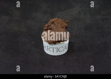 A scoop of chocolate ice cream in a white bowl with the word Arctica written on it. The bowl is sitting on a dark surface Stock Photo