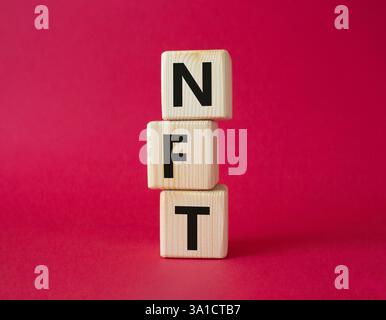 NFT - non-fungible token symbol. Concept word NFT on wooden cubes. Beautiful red background. Business and NFT concept. Copy space. Stock Photo