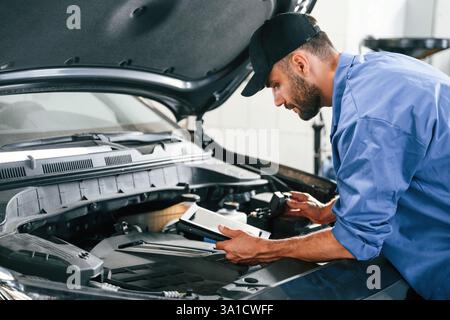 Using tablet. Auto mechanic working in garage. Repair service. Stock Photo