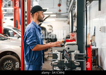 Standing by computer terminal. Auto mechanic working in garage. Repair service. Stock Photo