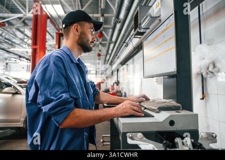 Side view, using computer. Auto mechanic working in garage. Repair service. Stock Photo