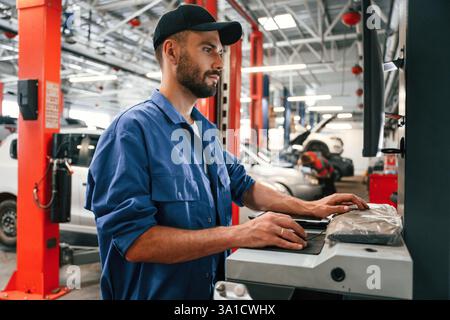 Side view, using computer. Auto mechanic working in garage. Repair service. Stock Photo