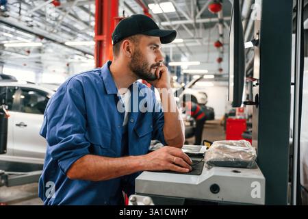 Side view, using computer. Auto mechanic working in garage. Repair service. Stock Photo