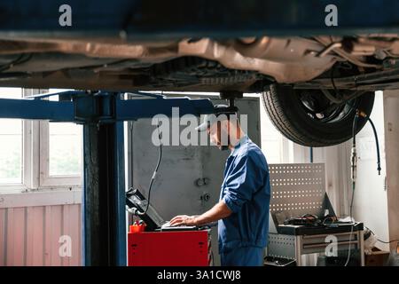 Using laptop and testing device. Auto mechanic working in garage. Repair service. Stock Photo