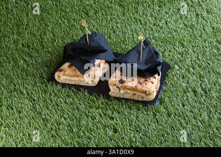 Two sandwiches with napkins on top of a green lawn. The sandwiches are cut in half and have a bite taken out of them Stock Photo