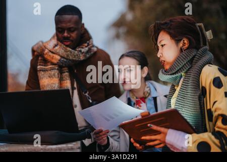 Multiracial people collaborating outdoors with documents and a laptop Stock Photo