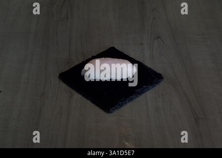 A piece of sushi is sitting on a black plate. The plate is square in shape and the sushi is placed on top of it Stock Photo